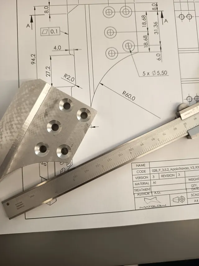 Peça maquinada em alumínio e paquímetro sobre um desenho técnico cotado